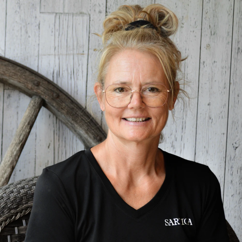 Femme souriante portant des lunettes devant un décor rustique